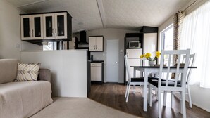Ein kompakter Wohnbereich mit Küchenzeile, einem Essbereich mit weißen Stühlen und einer Couch mit gemusterten Kissen.