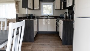 Eine kompakte Küche mit weißen und dunkelholzfarbenen Schränken, einer zentralen Kochinsel und einem Essbereich mit weißem Tisch und Stühlen.