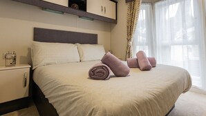 Ein ordentlich bezogenes Bett mit aufgerollten Handtüchern, ein Nachttisch mit einem Glasbehälter und ein eingebauter Kleiderschrank darüber.