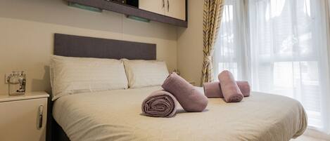 A neatly made bed with rolled towels, a bedside table with a glass container, and a built-in wardrobe above the bed.
