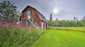 Ein rustikales Bauernhaus mit einer Holztreppe, die zu einer blauen Tür führt, umgeben von üppiger Vegetation und Wildblumen.