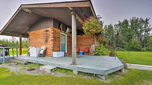 Eine rustikale Holzhütte mit überdachter Veranda, Sitzgelegenheiten im Freien und einem hängenden Blumenkorb.