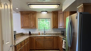 A kitchen with wooden cabinets, a stainless steel refrigerator, a microwave, and a window with a view of greenery.