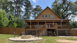 A wooden cabin with a porch, a staircase, and a fire pit.