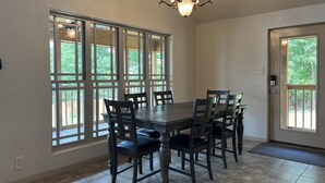 A dining area with a large table and chairs, large windows, and a chandelier.