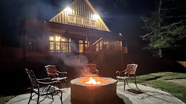 A stone fire pit with four chairs in front, surrounded by a concrete patio.