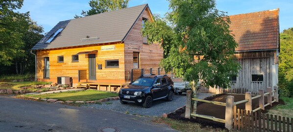 A wooden building with a sloped roof, a car parked in front, and a wooden fence.