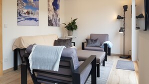 A modern living room with a sofa, armchair, and floor lamp. There are two wall-mounted paintings and a potted plant. - Fantastic chalet with outdoor WHIRLPOOL. NEW since 2024: outdoor SAUNA!!! (Gersfeld (Rhön))