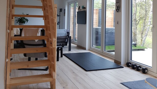 A spacious room with a wooden staircase, large windows, and a black exercise mat. - Fantastic chalet with outdoor WHIRLPOOL. NEW since 2024: outdoor SAUNA!!! (Gersfeld (Rhön))