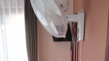 Quarto com uma mesa de jantar, televisão presa à parede, ventoinha no teto e janela com cortinas.