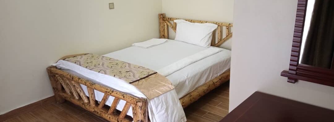 Una cama individual con estructura de madera, ropa de cama blanca y una manta estampada.