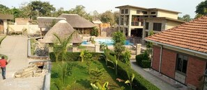 A resort with a swimming pool, thatched-roof structures, and a mix of modern and traditional architecture. - Bucolic Heritage Resort (Adjumani)
