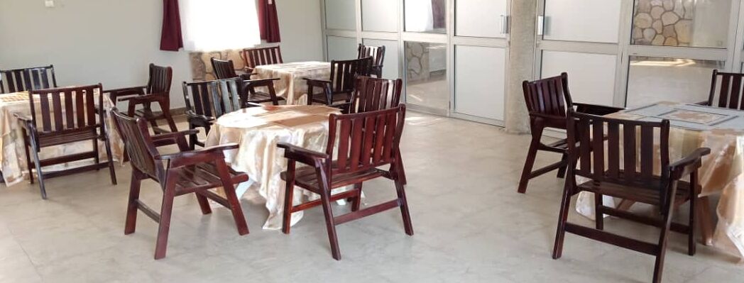 A dining area with round tables and wooden chairs, a stone wall, and a large window.