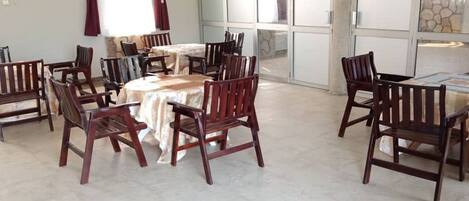 A dining area with round tables and wooden chairs, a stone wall, and a large window.