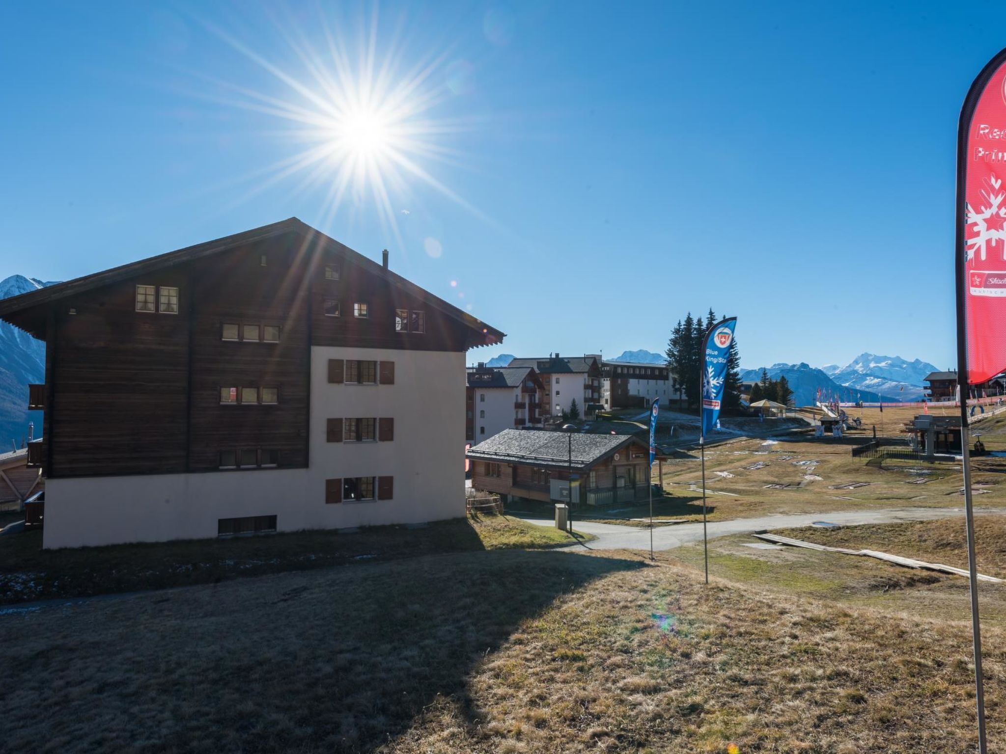 Ein Holzgebäude mit Satteldach, ein kleines Nebengebäude und ein freier Blick auf die Berge im Hintergrund.