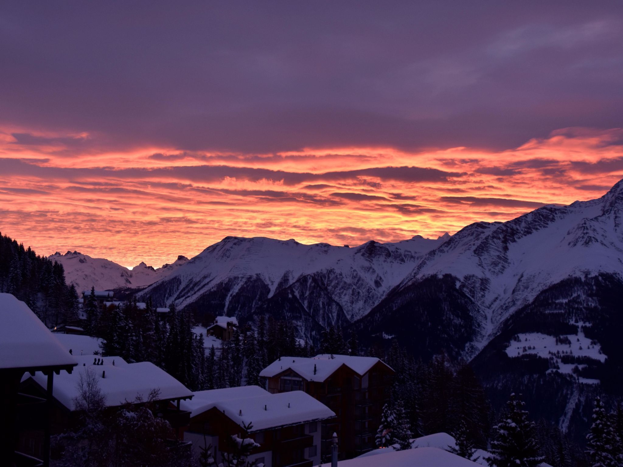 A mountain landscape with snow-covered peaks and a sunset sky.