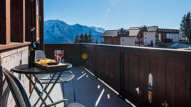 A wooden balcony with a table and chairs, overlooking a mountain range.