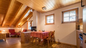 A cozy room with a wooden ceiling, a dining table with chairs, a red sofa, and a TV.