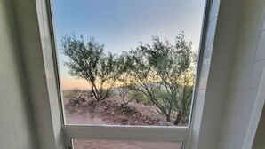 A bathroom with a large window, a bathtub, and a view of a desert landscape with sparse vegetation.