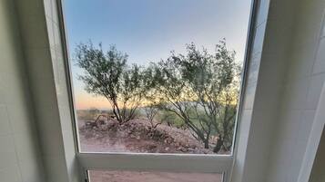 A bathroom with a large window, a bathtub, and a view of a desert landscape with sparse vegetation.
