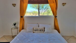 A bedroom with a bed, a bedside table with a vase, and a window with curtains.