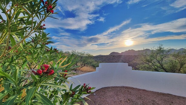 A desert landscape with a white structure, possibly a viewing platform, overlooking a range of hills and sparse vegetation.