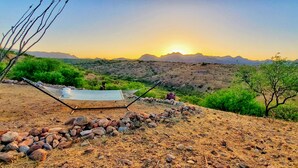 A hammock set up on a rocky terrain with a view of distant mountains and a sunset.