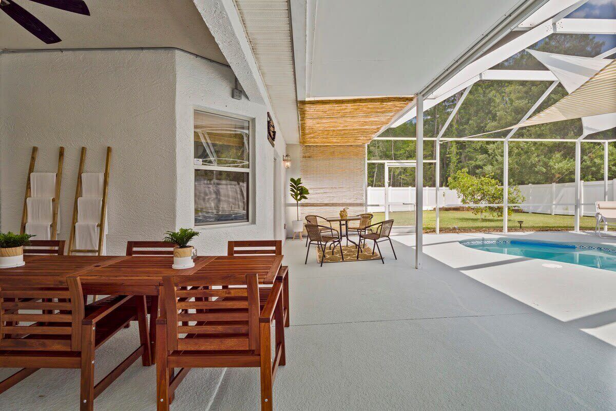 Ein moderner Essbereich im Freien mit einem Holztisch und Stühlen, einem kleinen runden Tisch ebenfalls mit Stühlen und einem Pool im Hintergrund.