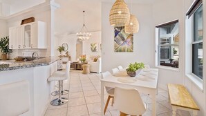 Una cocina moderna con armarios blancos, encimera de mármol y un comedor con mesa y sillas blancas.