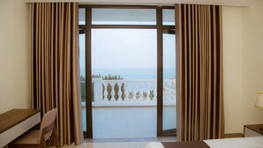 Une chambre d’hôtel avec un lit, un bureau et une chaise. Elle dispose d’un balcon avec vue sur la mer.