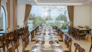 Une longue table à manger, entourée de chaises, dressée pour un repas, dans une pièce bien éclairée avec de grandes fenêtres.