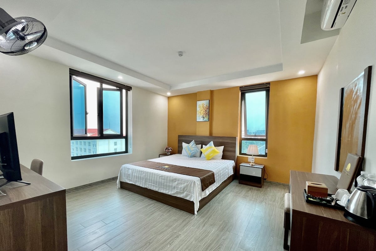 Quarto de hotel com cama, mesas de cabeceira, escrivaninha, cadeira e televisão.