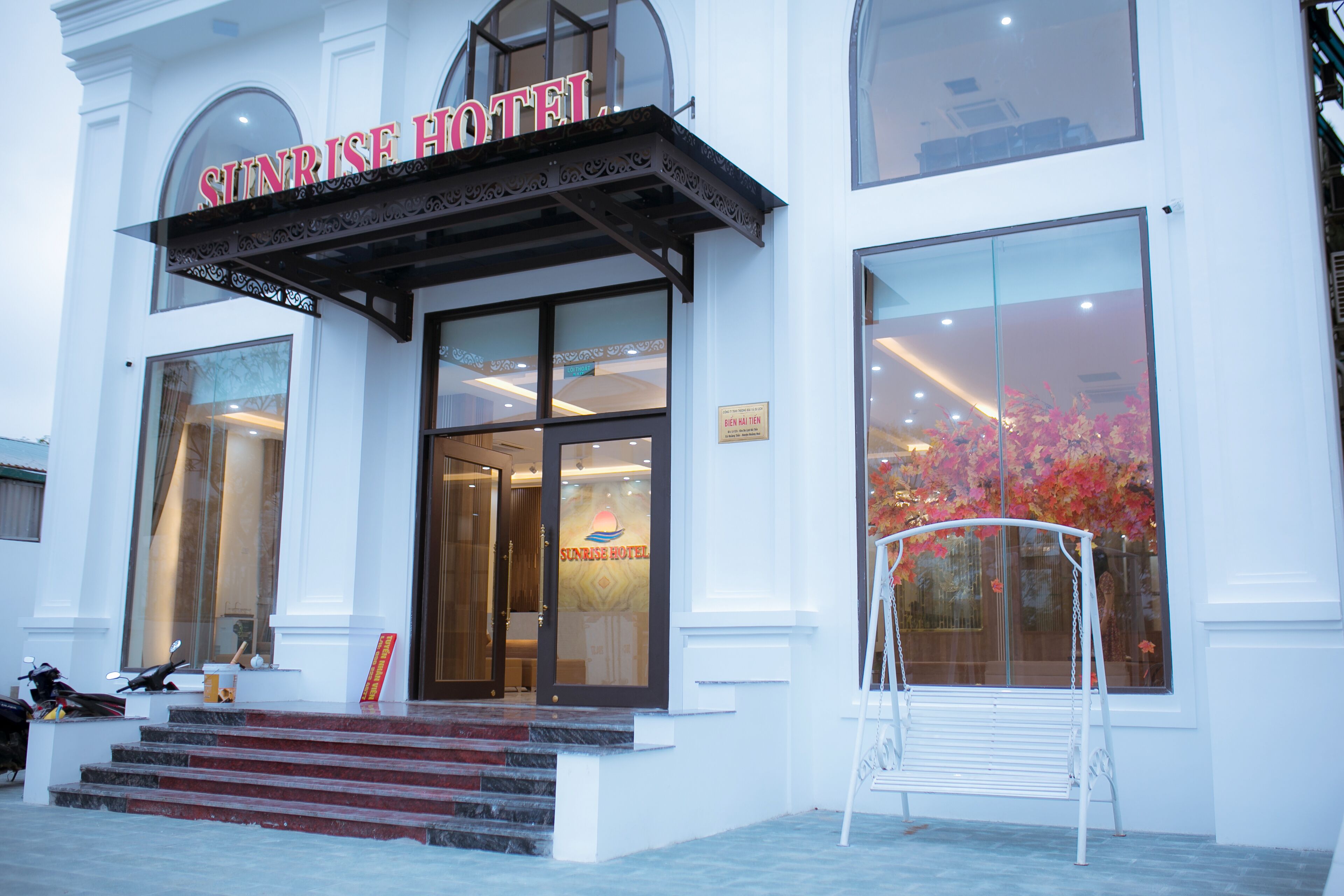 The exterior of the Sunrise Hotel with a prominent entrance, steps leading up to the door, and a bench outside.