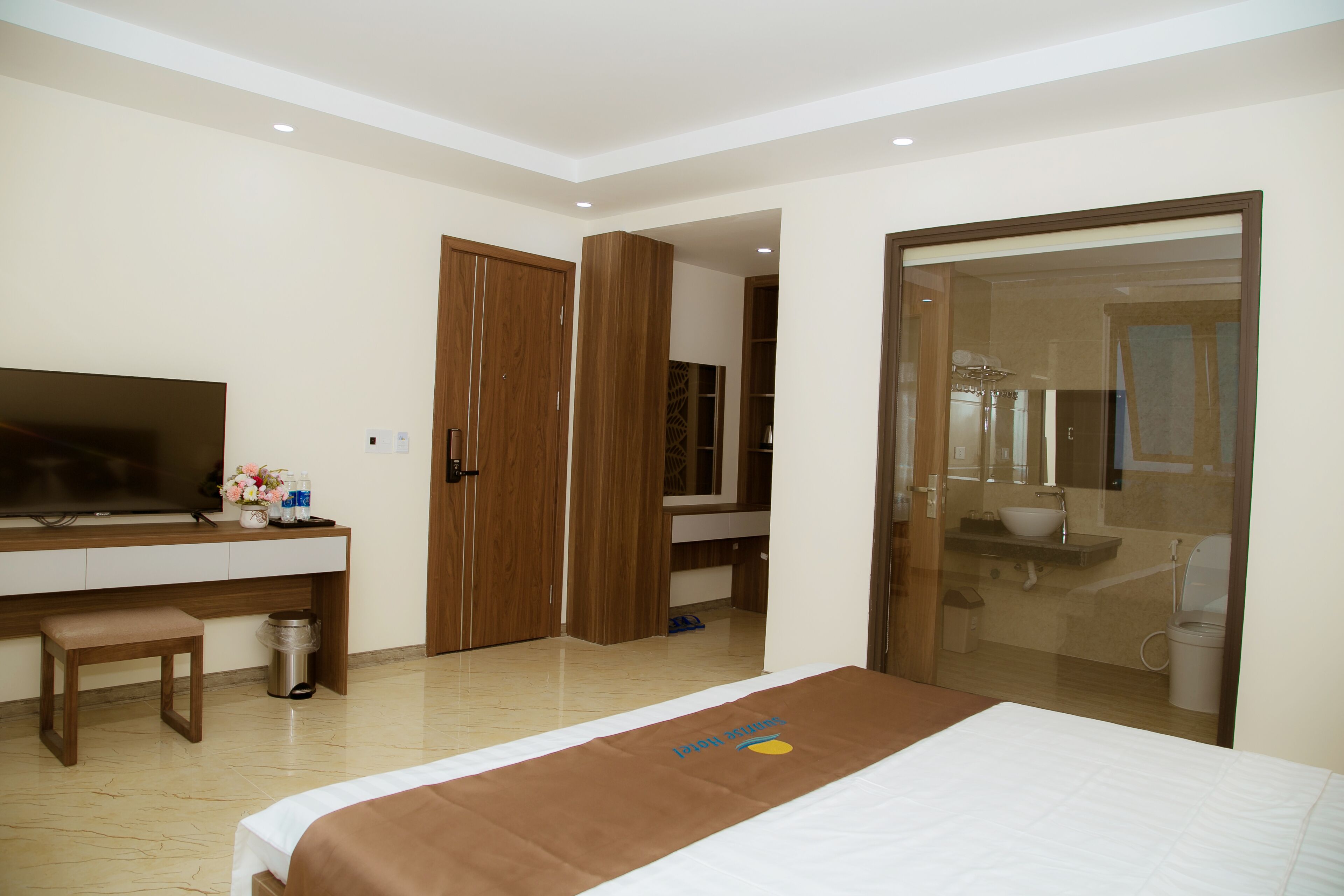 Une chambre d’hôtel comprenant un lit, un bureau, une télévision, un miroir et une salle de bain visible à travers une porte en verre.