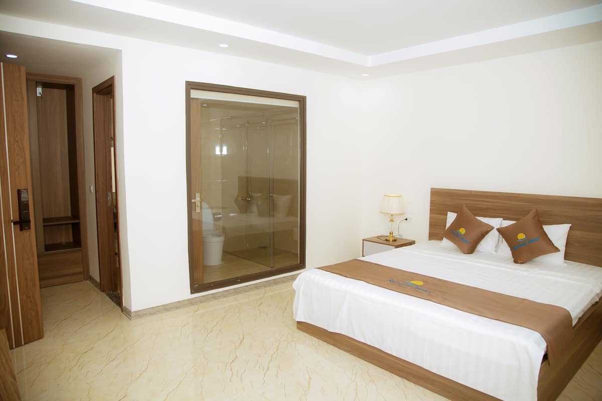 Quarto de hotel com uma cama grande, box de vidro e guarda-roupa de madeira.