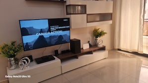 En moderne stue med et stort fladskærms-tv på et hvidt tv-møbel, en Galaxy Note20 Ultra 5G smartphone og dekorative genstande.