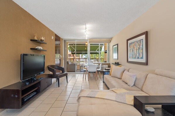 A modern living room with a flat-screen TV, a sofa, a coffee table, and a dining area with chairs and a table.