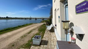Aussicht auf einen Fluss mit einer Brücke im Hintergrund, ein weißes Gebäude mit einem Schild, Außenbereich zum Sitzen und einer Blumenkiste.