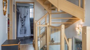 Eine Holztreppe mit Glasgeländern führt zu einem Raum mit einem Spiegel, einem gerahmten Bild und einem kleinen Tisch.