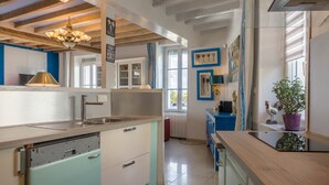 Eine Küche mit Spüle, Geschirrspüler und Holzbalkendecke. Ein Fenster mit blauen Vorhängen und ein Topf mit Pflanze stehen auf der Arbeitsplatte.