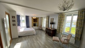 Ein Schlafzimmer mit einem Bett, einem Schminktisch, zwei Stühlen, einer Chandelier und Blick ins Freie.