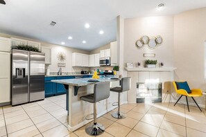 A modern kitchen with a central island, bar stools, a refrigerator, and a microwave.
