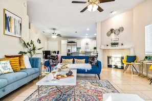 A modern living room with a blue sofa, a coffee table with a fruit platter, and a colorful rug.