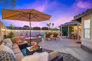A cozy outdoor patio with a sofa, chairs, a table with fruit, and a hot tub.