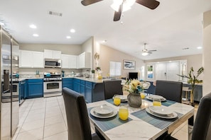 A modern kitchen with blue cabinets, a dining area with a table set for two, and a ceiling fan.
