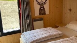Ein gemütliches Blockhausszimmer mit zwei Betten, einem großen Fenster mit Vorhängen und einem Bild von einem Reh an der Wand.