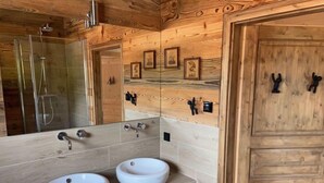 Ein Badezimmer einer Holzhütte mit zwei Waschbecken, einer Dusche und einer Tür mit schwarzen Griffen.