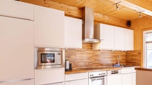 A modern kitchen with white cabinetry, stainless steel appliances, and a wooden ceiling. - Premium #18 mit Sauna&Sprudelbad by Interhome (Hohentauern)
