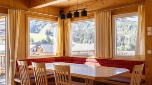 A wooden dining area with a large table and chairs, large windows with curtains, and a view of a forested area. - Premium #18 mit Sauna&Sprudelbad by Interhome (Hohentauern)