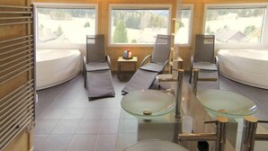 A room with two curved beds, a glass table, and a view of a snowy landscape. - Premium #18 mit Sauna&Sprudelbad by Interhome (Hohentauern)